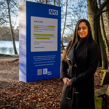 Harmeet stands in front of the NHS Talking Therapies public display in Black Park